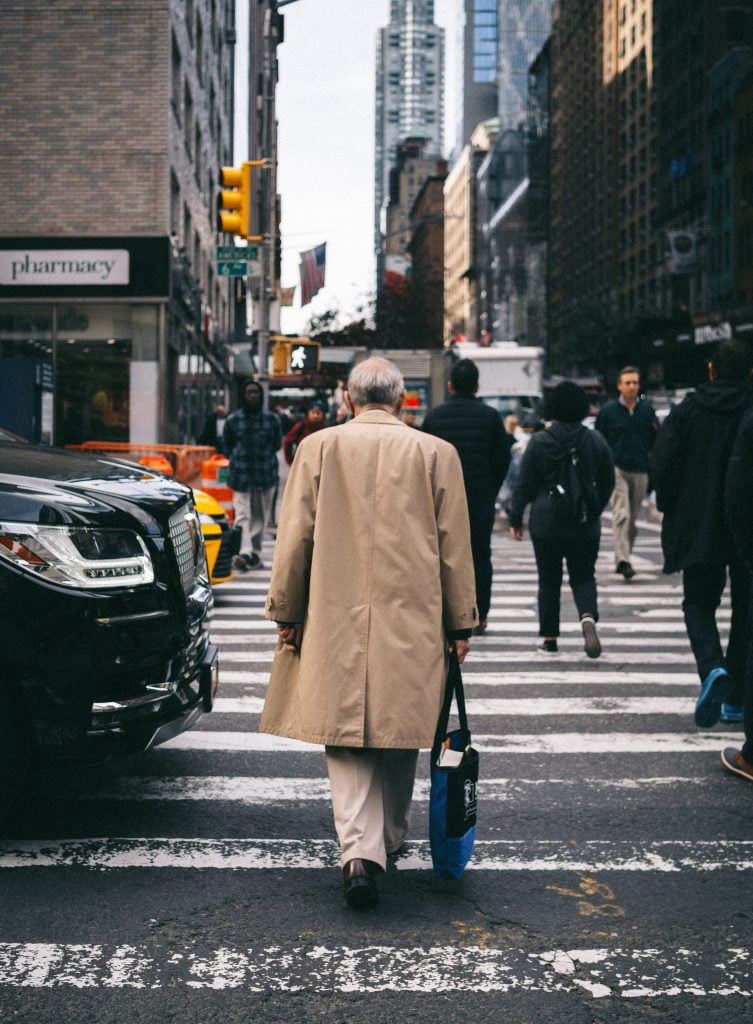 imagem representando o aumento e envelhecimento da população, há um homem idoso atravessando a rua em meio a cidade